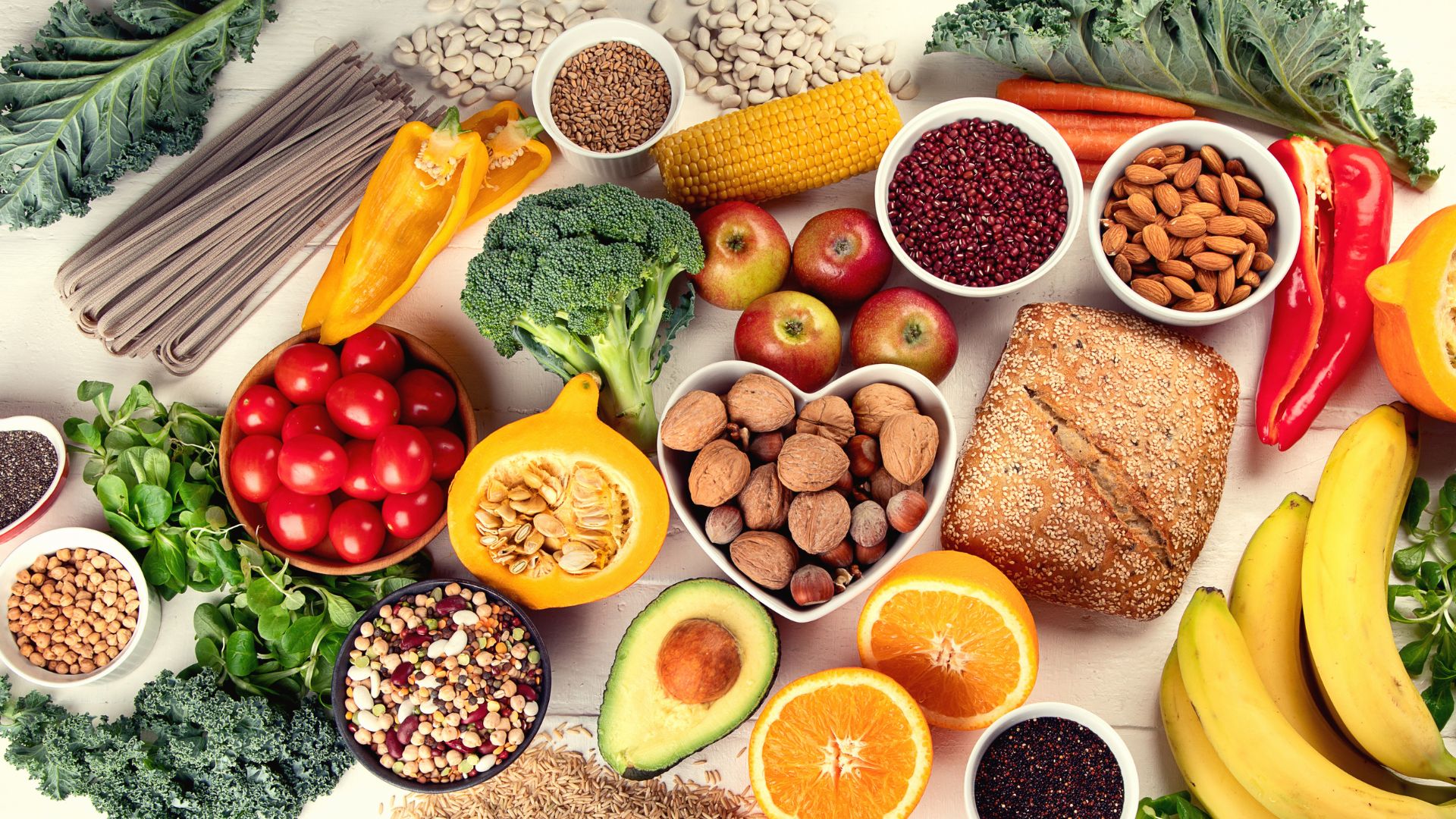 Selección de alimentos saludables ricos en fibra y antioxidantes como frutas, verduras, frutos secos, legumbres y cereales integrales sobre una mesa clara.